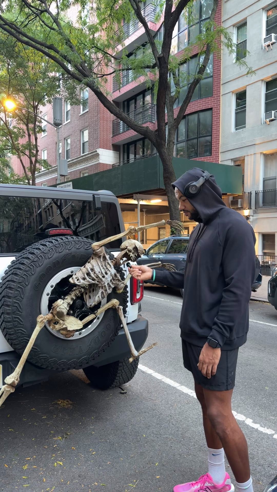 Inspecting a fake skeleton zip-tied to a truck's spare tire on a city street
