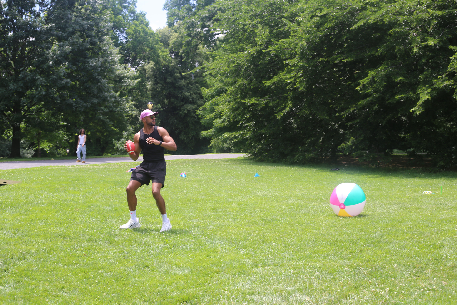 Mid-catch with a football in a park, giant beach ball in the background