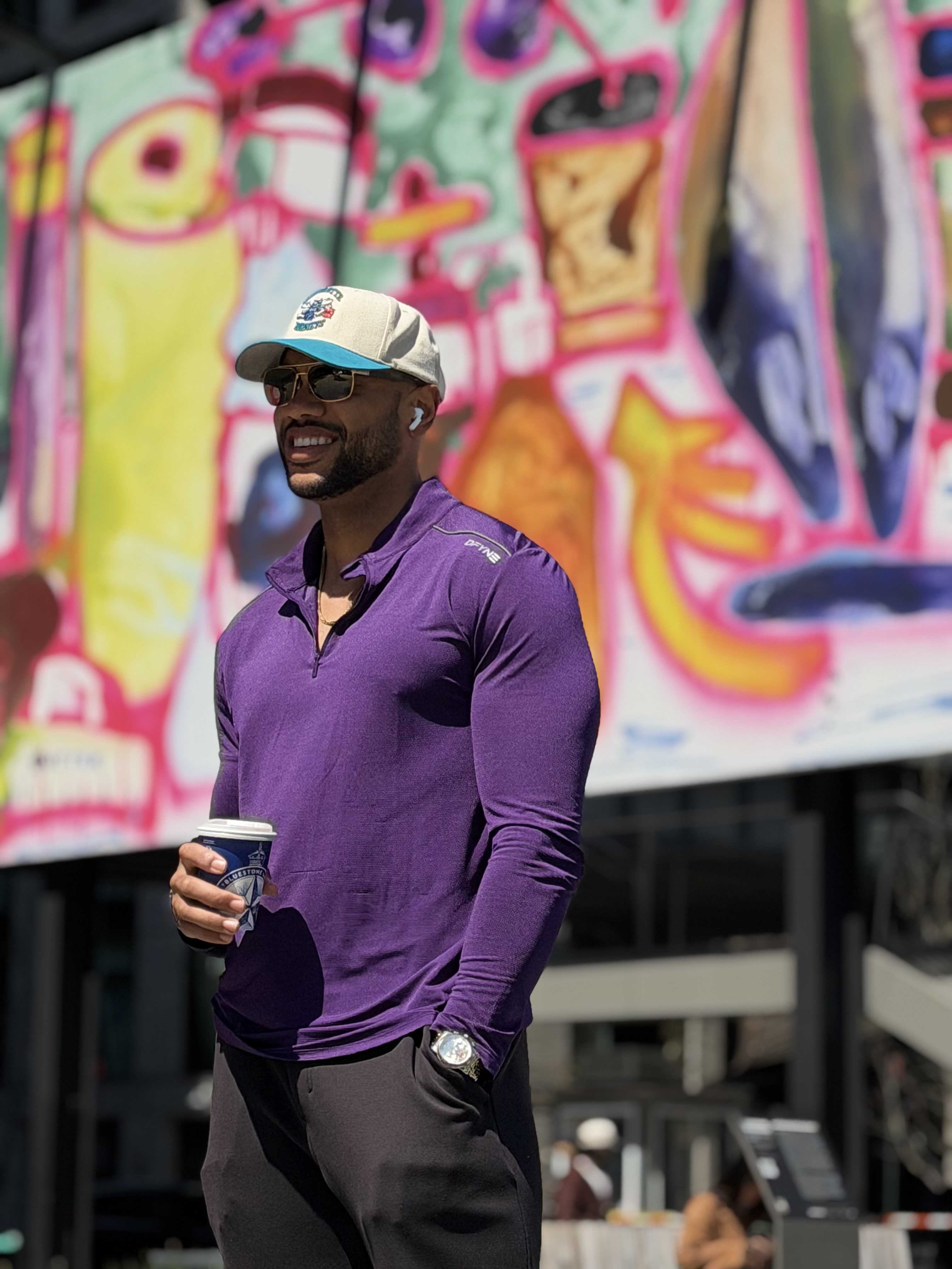 Holding a coffee in front of a mural, looking unreasonably pleased about it